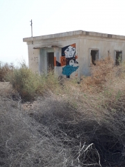 Abandoned military structure with desert bushes and female mural. Kalya